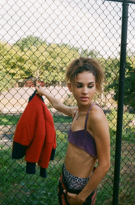 By a chain link fence, red jacket in hand, Lala Olsson by David Spector