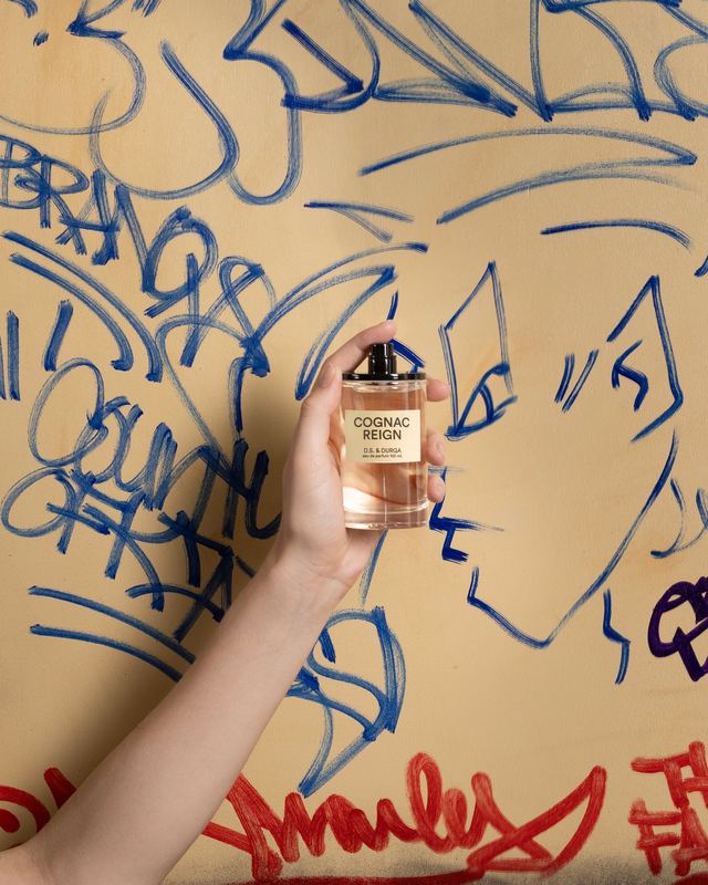 A hand holding the bottle to a graffiti wall, Cognac Reign by David Spector