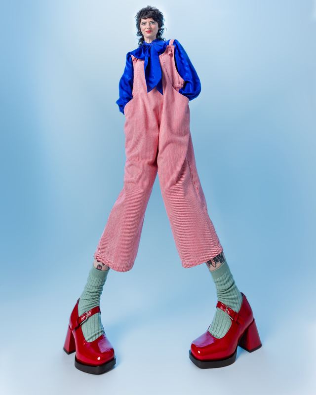 Pink overalls and red platforms on blue, Sarah Squirm by David Spector